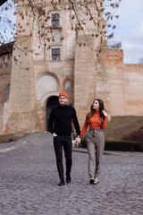 Beautiful Tourist Couple In Love Walking On Street Together. Happy Young Man And Smiling Woman Walking Around Old Town Streets, Looking At Architecture. Travel Concept.
