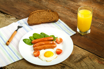 Fried eggs with sausages and tomatoes with bread on a napkin and a glass of juice.