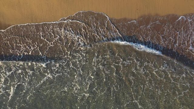 Aerial footage of turquiose sea waves breaking on sandy coastline. Sunny summer day at the beach