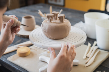 Closeup of bottom of mug, which is being decorated in ceramic studio. Female professional hands making clay dots or drops on the surface of vase by special squeezing tool.