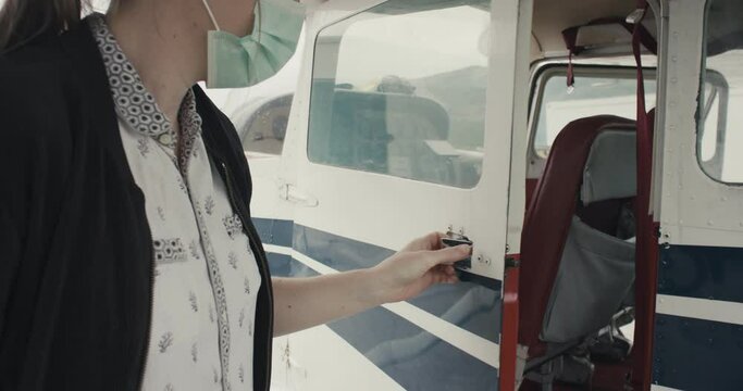 Woman with face mask opens doors cockpit of small airplane plane aircraft learning for a pilot during virus covid 19 coronavirus pandemic outbreak new normal