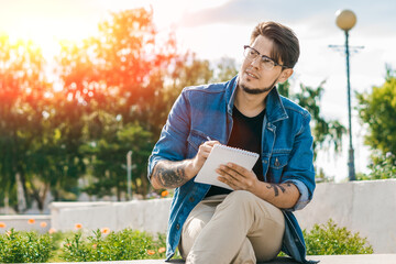 Obraz premium Young handsome freelancer writing in notebook outdoors. Outdoor work concept.