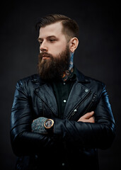 Portrait of a tattooed cool bearded man in a leather jacket with arms crossed
