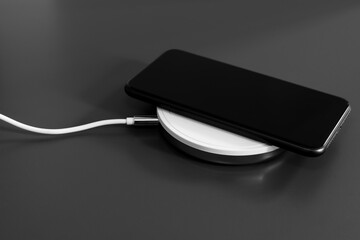 Close-up of a black mobile phone charging on a white wireless charging device