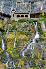 Fototapeta na wymiar Buildings and waterfalls on a steep limestone cliff where the St. Beatus Caves are located, Switzerland 