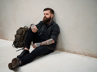 Travel and education concept. Bearded hipster guy with backpack sitting on a floor in studio