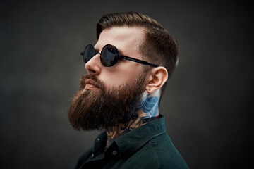 Closeup portrait of a cool bearded male in sunglasses on a dark background