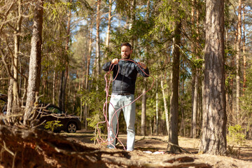 young man with a rope in his hands stands in the forest