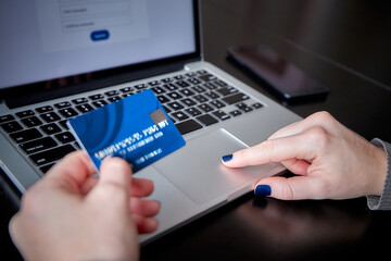 Close-up of caucasian woman's hands with blue nails typing on her computer with credit card and smartphone, for online shopping concept