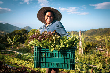 Portrait of proud organic farmer woman wearing a hat from a quilombola community harvesting vegetables. Bio food gathering in a sunny day and blue sky.