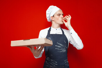 baker holds pizza and shows gesture of good taste on a red isolated background, guy in the form of...