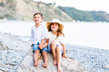 little boy and girl sitting on the sea beach holding hands and smiling