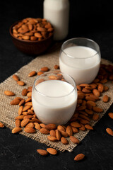 almond milk with glasses on sprinkled nuts, vegetarian milk drink without lactose against a dark background, close-up