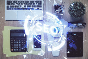 Double exposure of SEO hologram drawing over desktop. Top view. Search optimization concept.