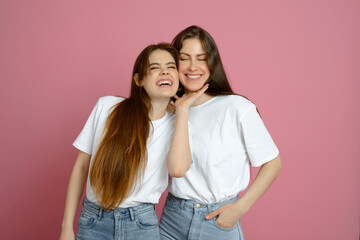 young happy sisters smiling on pink background