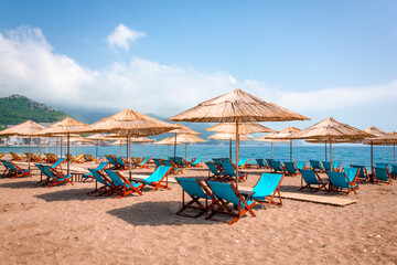 Thatched beach umbrellas and stylish sun loungers on Becici beach in Budva. Beach season on the Adriatic