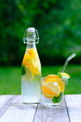 Fruit infused water, summer cocktail, detox drink with lemon, orange slices and mint in glass and bottle on rustic wooden table.