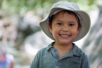 Young hispanic boy wearing a fishing hat that is smiling and looks happy in a natural outdoor setting.