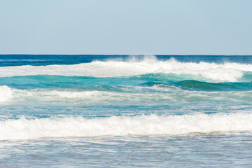 Ocean waves with white foam splashes on a bright sunny day. Background with copy space