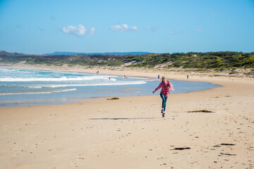 A girl skipping on a scenic beauriful sandy Bendalong Beach on sunny winter day. Bendalong, NSW, Australia.