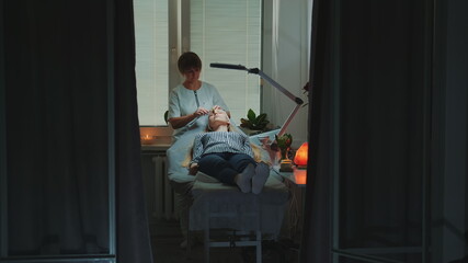 Dolly shot of Beautician making relaxing facial massage with jade roller on woman's face at beauty...