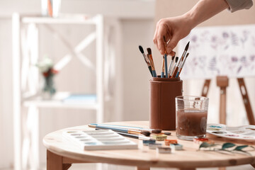 Fototapeta na wymiar Watercolorist taking brush from holder on table in workshop, closeup