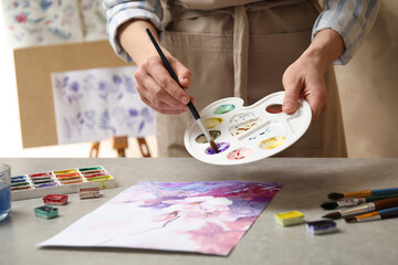 Plakat Woman painting flowers with watercolor at grey stone table in workshop, closeup