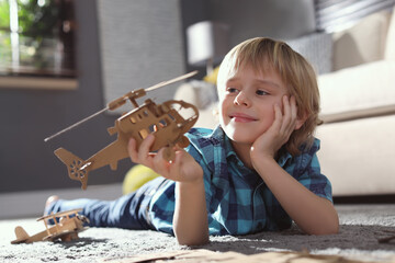 Little boy playing with cardboard helicopter on floor at home. Creative hobby © New Africa