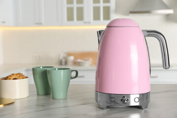 Modern electric kettle, cups and cookies on table in kitchen