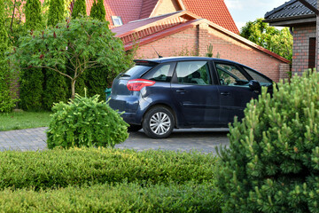 Fragment of a car parked near the garage on the background of garden. Selective focus.