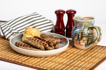 grilled breakfast sausages and a biscuit with a cup of coffee on a bamboo mat
