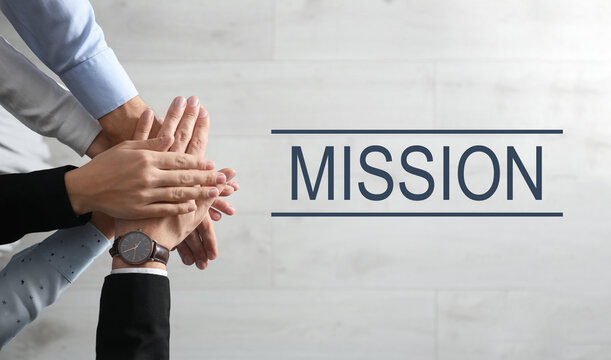 People holding hands together over light wooden background and text MISSION, top view