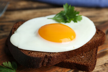Tasty fried egg with parsley and rye bread on wooden board, closeup