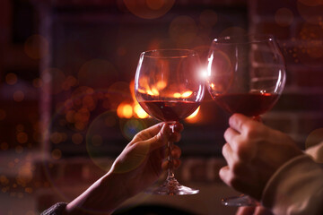 Lovely couple with glasses of wine near fireplace indoors, closeup. Winter vacation