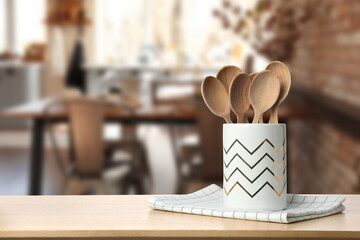 Holder with spoons and towel on wooden table in kitchen. Space for text