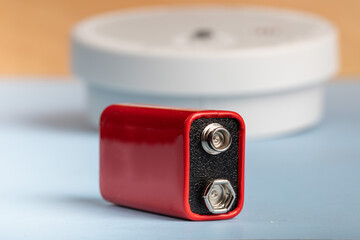 a 9 volt battery with a home smoke alarm in the background