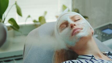 Medium close-up shot of professional facial skin care treatment with a cosmetic steamer at beauty salon. The Steam cleaning procedure of the face. - obrazy, fototapety, plakaty