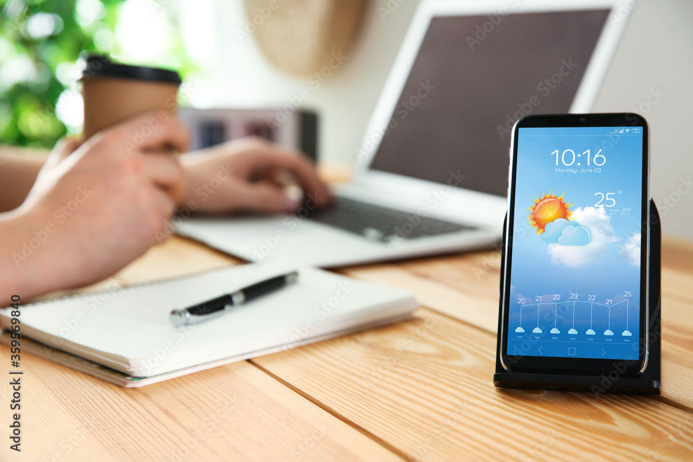 Wall mural man working at table and smartphone with open weather forecast app indoors