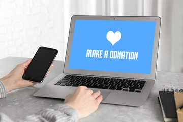 Donations concept. Woman with smartphone working on laptop at table, closeup