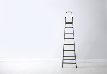 Modern metal stepladder near white wall. Space for text
