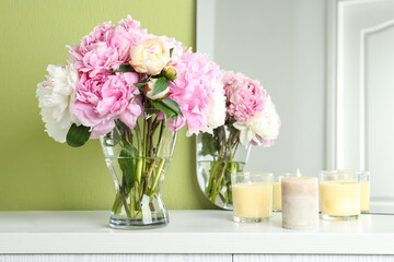 Beautiful peonies and candles on white dressing table near green wall