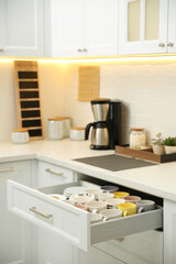 Fototapeta premium Open drawer with cups and coffeemaker on countertop in kitchen