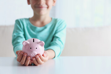 Little boy with piggy bank at white table indoors, closeup. Space for text
