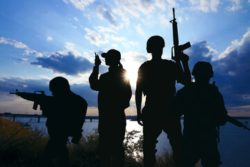 Fototapeta na wymiar Silhouettes of soldiers with assault rifles and portable radio transmitter patrolling outdoors. Military service