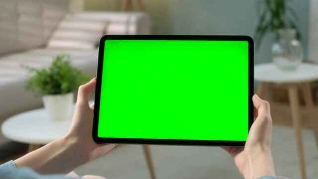 Point of View View Young Woman at Home Sitting on a Chair Using With Green Mock-up Screen Tablet. Girl Using Touchscreen Device, Browsing Internet. Concept of Green Screen and Chroma Key.