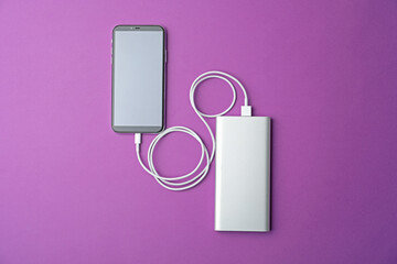 Smartphone and portable charger on purple background, flat lay. Modern technology