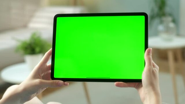 Point of View of Woman Using Hand Gestures on Green Mock-up Screen Digital Tablet Computer in Landscape Mode while Lying on a Sofa. In the Background Cozy Living Room.