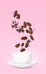 Cocoa beans falling into cup on pink background