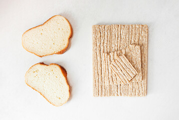 Different types of bread, white yeast bread and healthy crispbread on a white cement table, top view