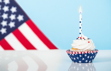 Patriotic 4th of July cupcake and a candle. Light blue background with American flag. 